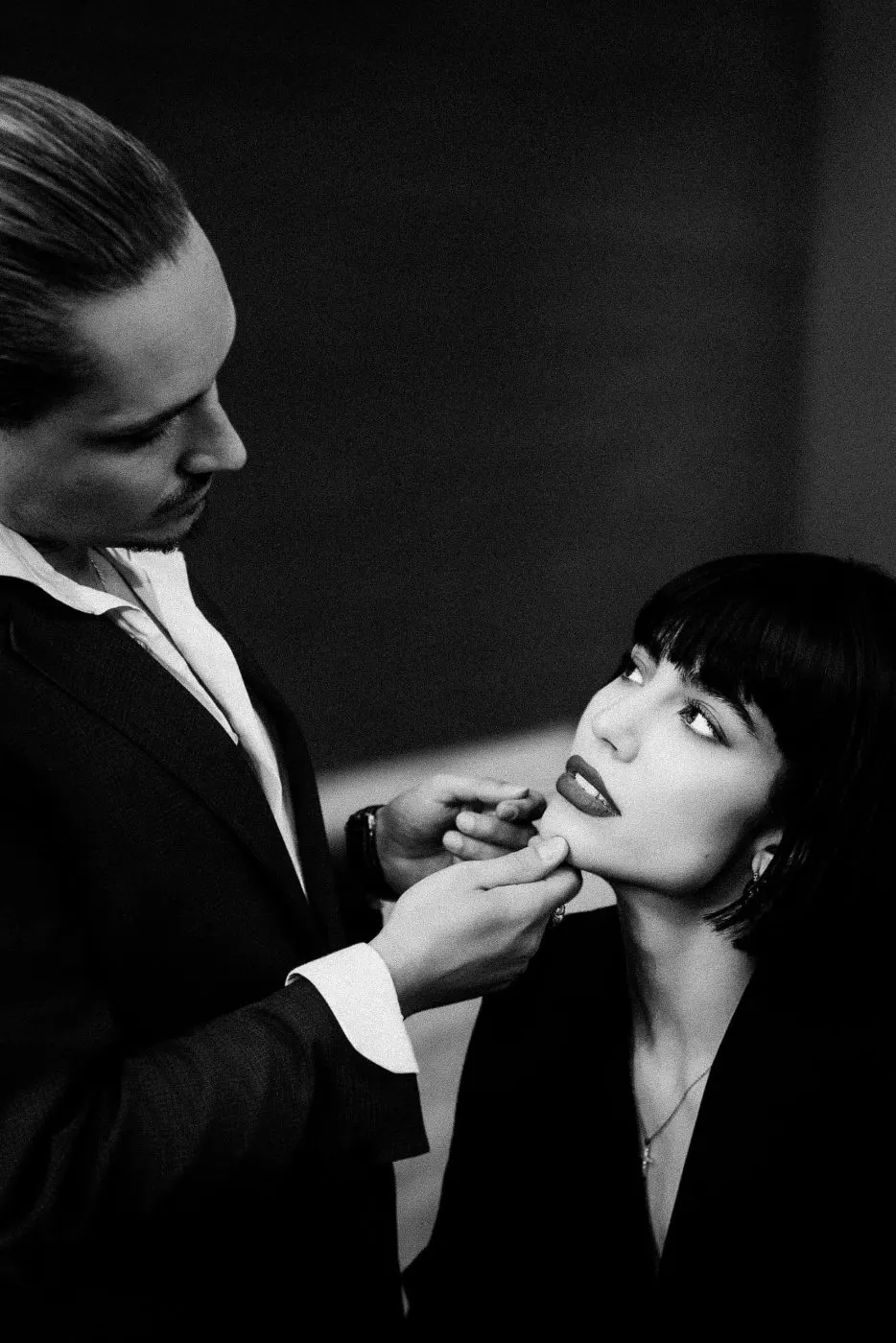 The hairdresser lifts her chin gently, her gaze meeting his.